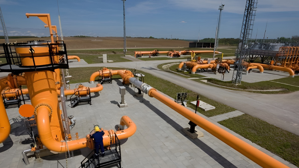 Hydrogen pipeline facility with orange gas pipes and worker inspecting equipment outdoors.